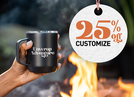 Black camp mug being held beside a fire with text to the right which reads "25% off Customize"