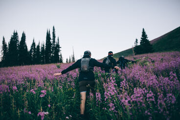 Three hikers with hydration packs walking through a field of flowers. 