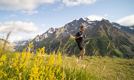 Man walking up a trail with a mountain range in the distance.