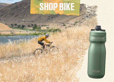 Man riding a bike through a field with Podium Steel bottle
