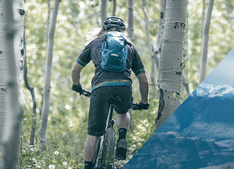 Man biking through birch trees wearing a Mule 12 hydration pack.