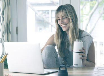 Woman drinking from a Multibev bottle and looking at a laptop.