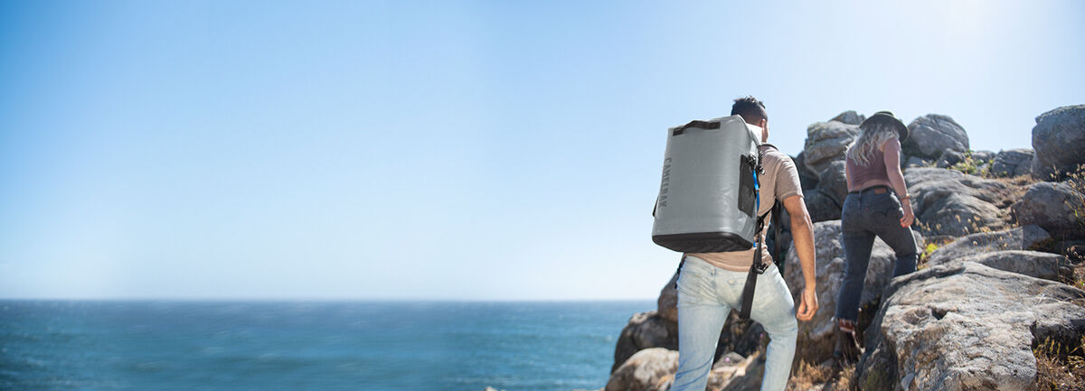 Two hikers with ChillBak coolers on their back, going up a seaside trail.