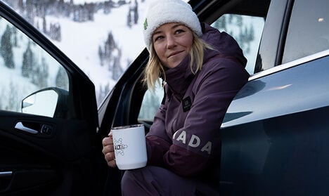 A customized camp mug being held by a woman at the base of a snowy mountain.