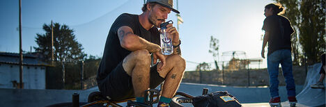 Guy taking a break on his BMX bike and drinking from his Eddy+ water bottle.