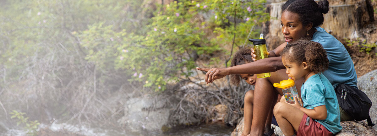 Chelsea Murphy pointing out something in the distance to her young daughter sitting next to her on a rock outside.