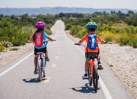 Two children riding their bikes with Mini MULE hydration packs. Two children riding their bikes with Mini MULE hydration packs.