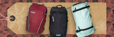 Three hydration packs in front of a holiday themed hang tag with wrapping paper in the background.