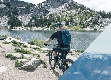 Man biking by a pristine lake wearing a blue CamelBak hydration pack.