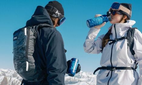 Two skiers at the top of a mountain taking a sip from their POW Limited Edition drinkware while wearing a POW Snow Pack.