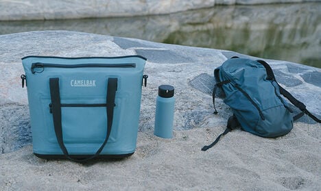 A Chillbak Cooler sitting on a beach with a water bottle and hydration pack