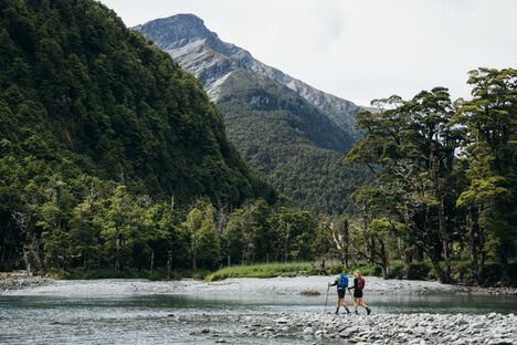 2 hikers wearing Rim Runner packs hiking through a river valley in the mountains
