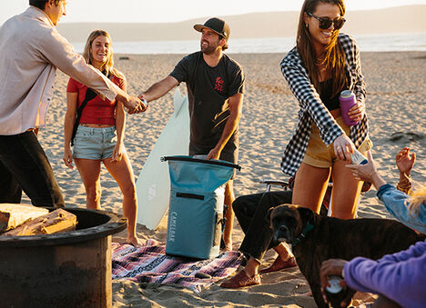 A guy handing out drinks on the beach with friends.