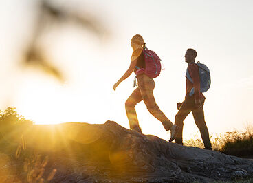 Two hikers going up a mountain with the sun setting ahead of them.