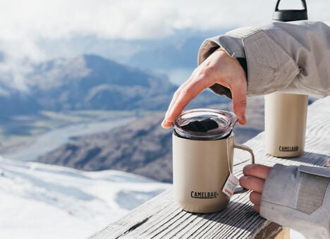 Snowy Mountain background with a Camp Mug sitting on a railing and multibev behind it.