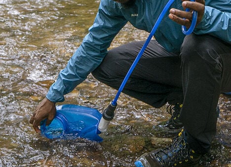 Man filling hydration pack water bladder from a river. 