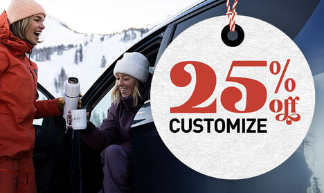 Person holding a customized camp mug while sitting in her car at the bottom of a snowy mountain.