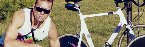 Retro picture of a guy posing beside his road bike in 90's CamelBak gear.