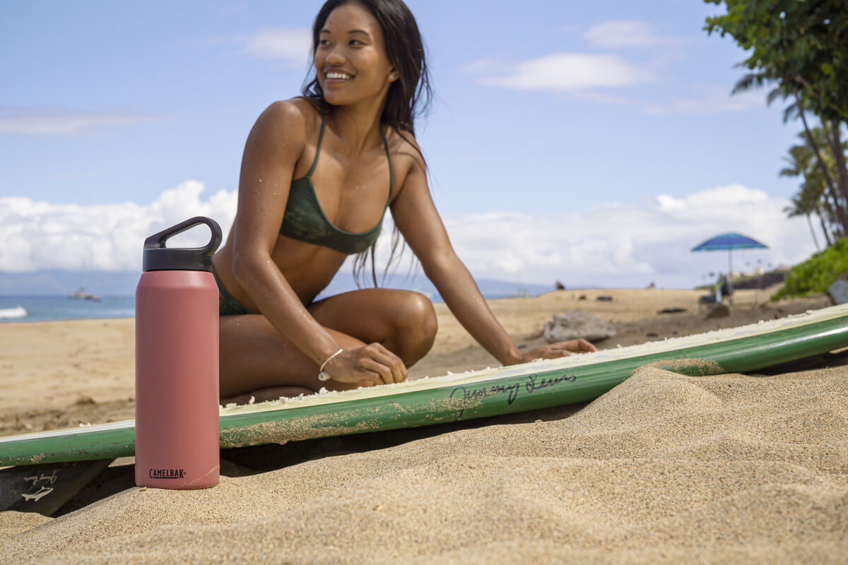 Woman with surfboard next to a stainless steel water bottle. Woman with surfboard next to a stainless steel water bottle.