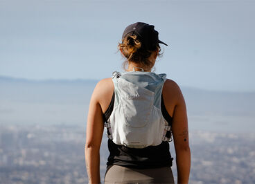 Runner with a hydration vest on at the top of a scenic view.