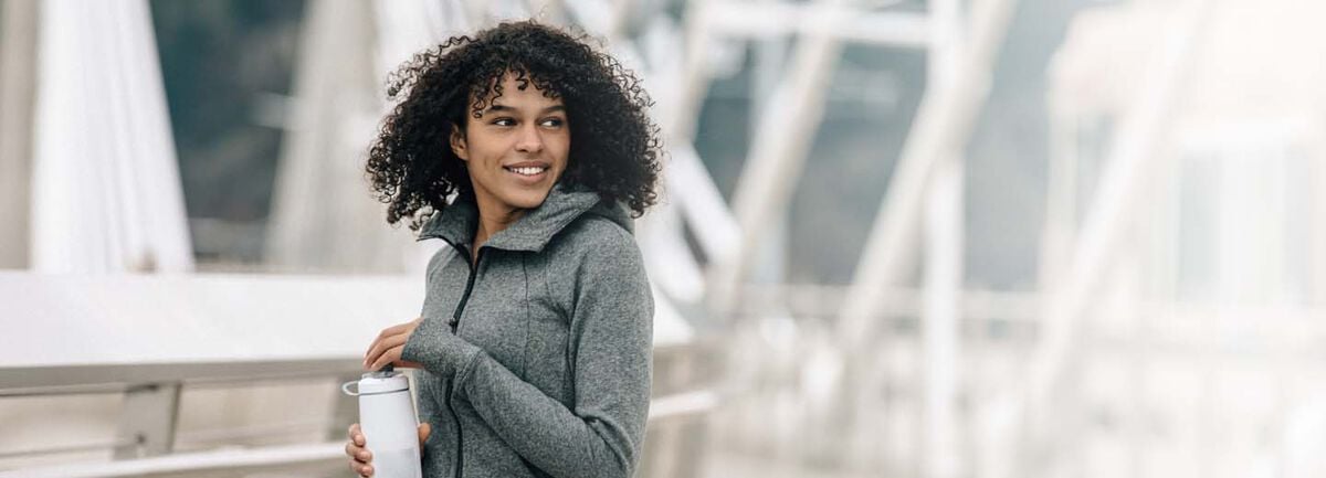 A women outside in an athleisure jacket with a white Podium bottle in her hands.