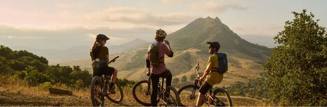 Three bikers on top of a mountain with the sun setting in the distance