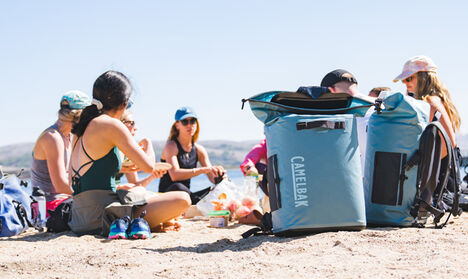 People sitting on sand at the beach with a soft cooler.