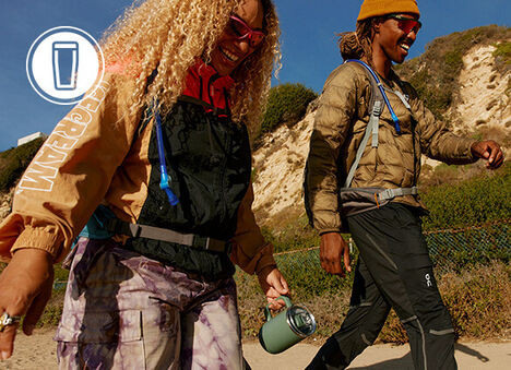 Two people walking down a trail with hydration packs on and a Thrive Tumbler mug.
