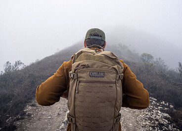 Man hiking on a foggy mountain trail with a coyote tan pack.