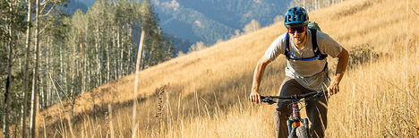 Mountain biker going down a trail with the mountains and a field behind him