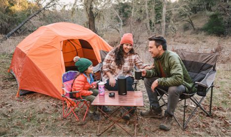 A family sitting around their campsite with a kids eddy+ bottle, 64oz carry cap, and camp mug in hand.