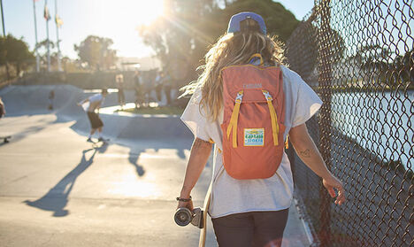 Woman with a new Arete 18 Hydration Pack walking along a fence line at a skate park.