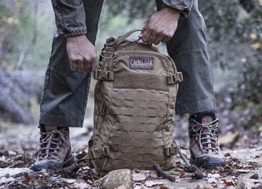 man opening a gmi backpack on a leafy trail