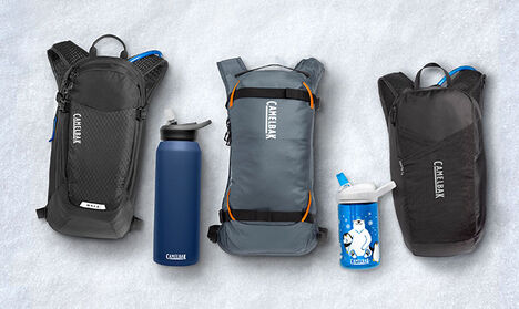 Three CamelBak Packs laying out with two bottles on a white blanket background.