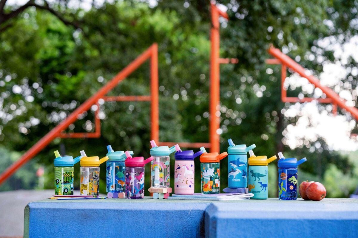 Ten limited edition kids Eddy+ 14oz water bottles in a row on a playground
