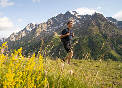 Man walking up a mountain trail with a hydration pack on.