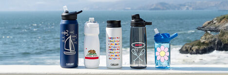 Five custom bottles sitting on a ledge with the ocean in the background.