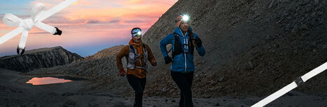 Two runners with headlamps on, running down a trail in the evening.