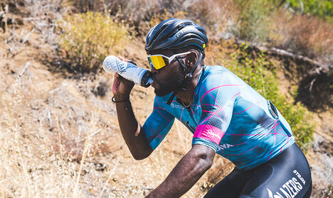 Cyclist riding bike in the mountains drinking from a podium water bottle Cyclist riding bike in the mountains drinking from a podium water bottle