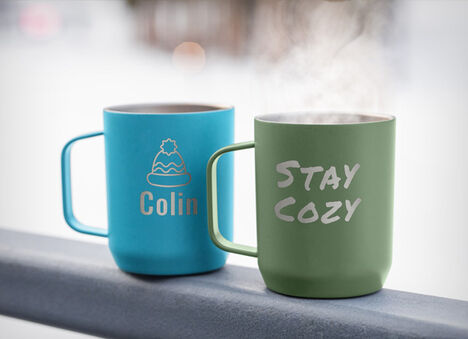 Two Horizon Camp Mugs laser engraved with text and logo sitting on a railing. Two Horizon Camp Mugs laser engraved with text and logo sitting on a railing.