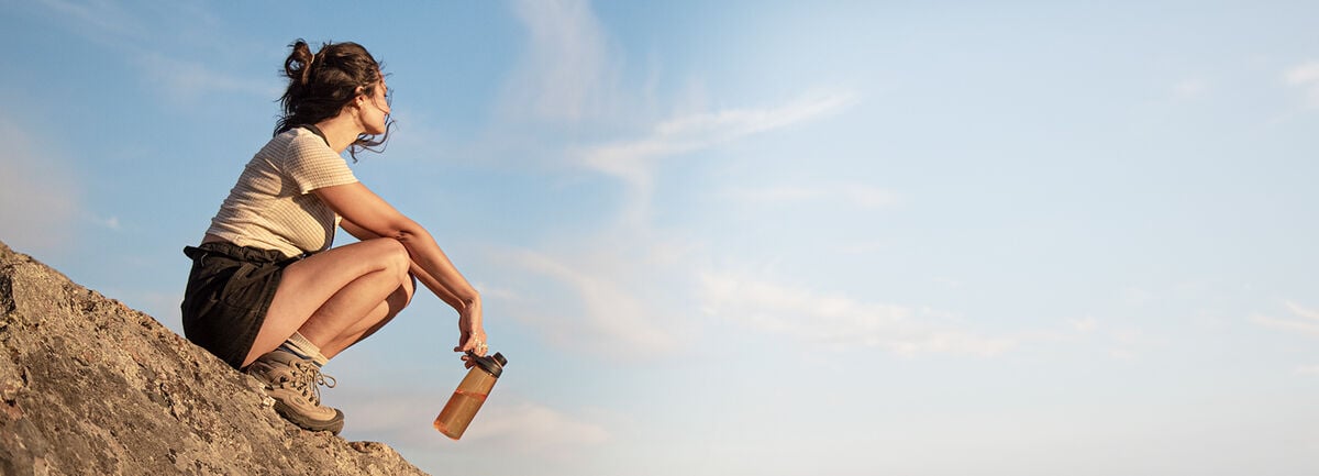 Woman sitting on a hill with a tritan renew bottle in hand.