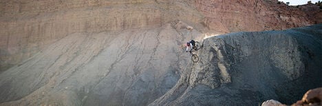 Biker going off a big downhill slope with a cliff behind him.