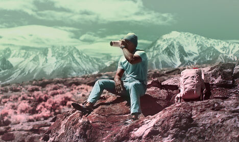 Cliford Mervil sitting on a rock drinking from a water bottle.
