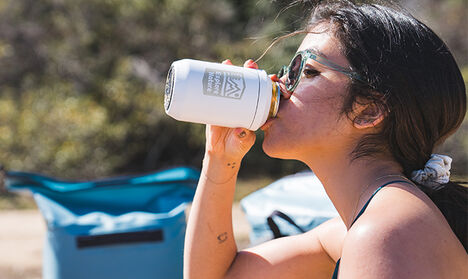A customized can cooler being used by a girl on the beach.