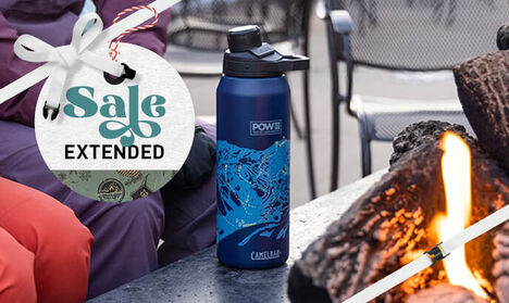 A 32oz POW Chute Mag Water Bottle sitting on a table with a fire to the right and skiers to the left.