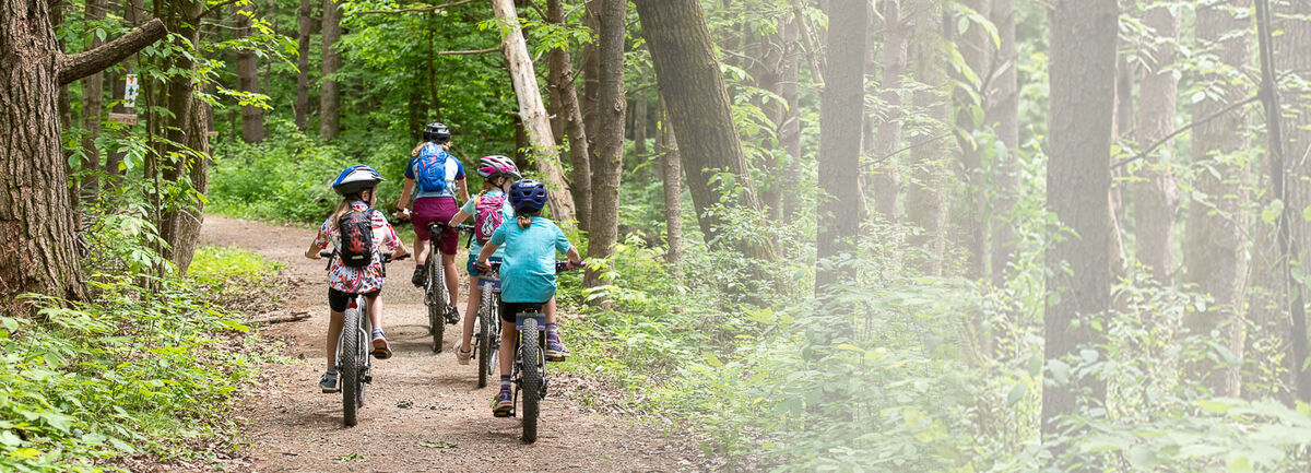 Women on bike leading 3 little girls on bikes on a trail in the woods. Women on bike leading 3 little girls on bikes on a trail in the woods.