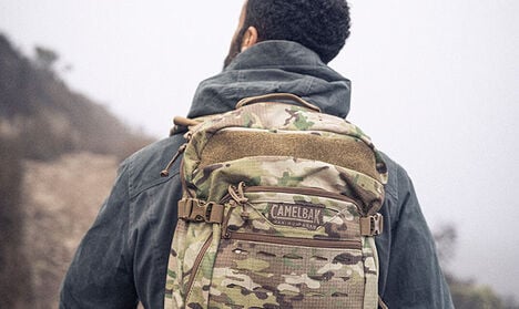 Man hiking with a camo hydration pack.