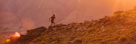 Runner going up a rocky trail with the sun shining over the ascent.