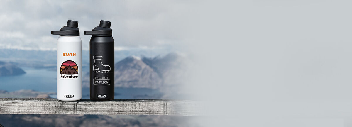 Two CamelBak custom bottles sitting on a ledge with a snowy mountain behind them.