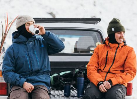Two skiers on the bed of a truck, drinking from their VSS drinkware.